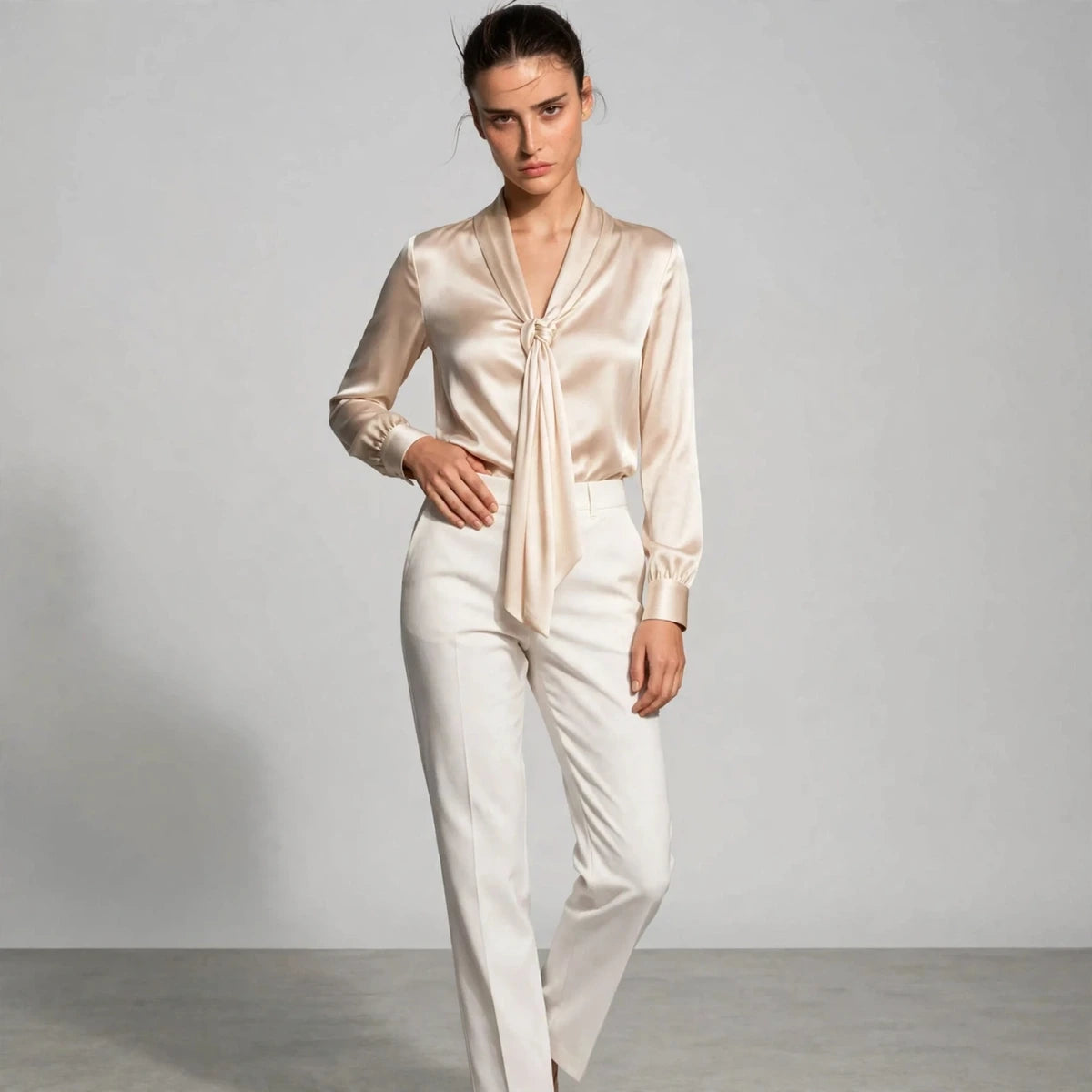 Model wearing beige satin tie-neck blouse with white trousers in a fashion editorial