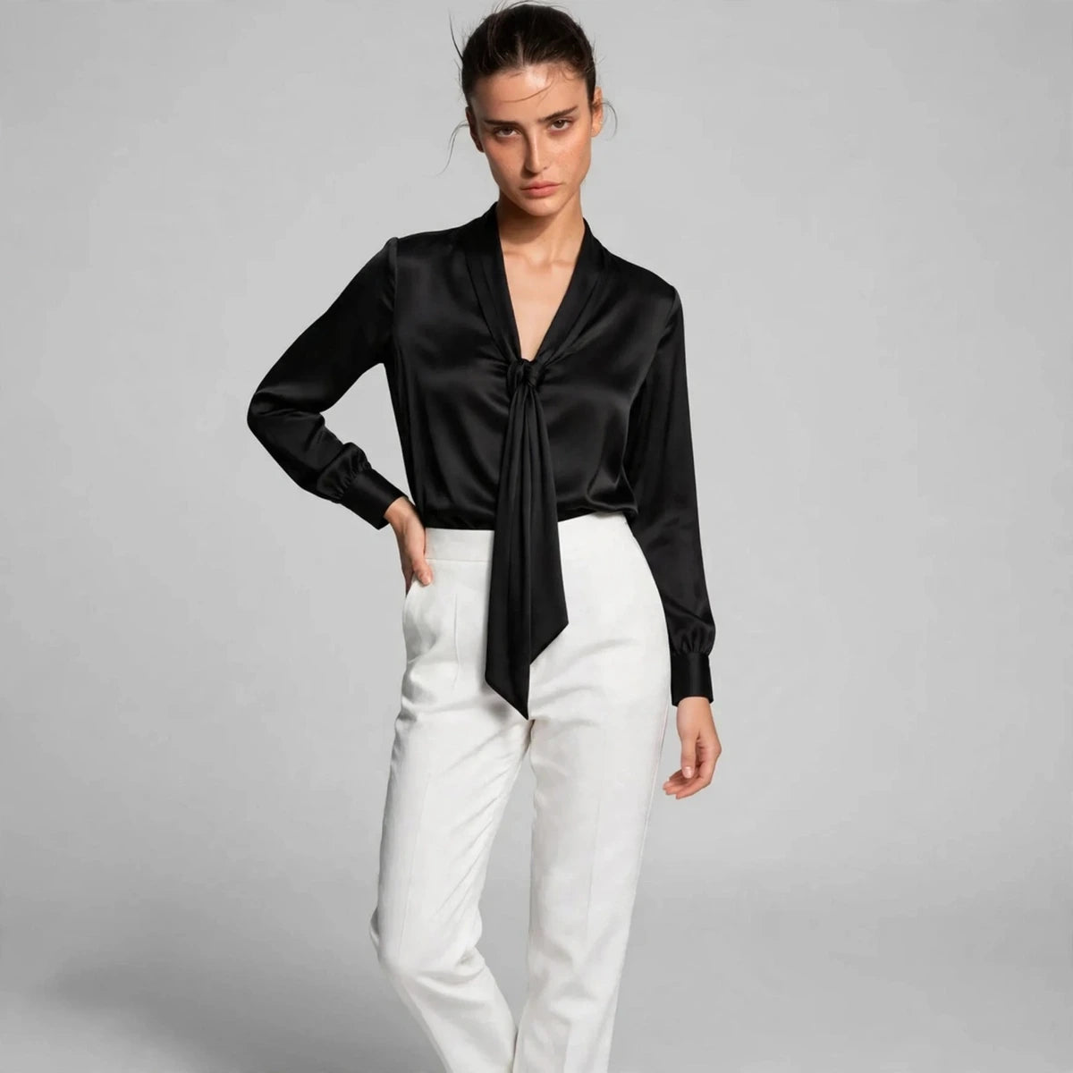 Model wearing black satin tie-neck blouse with white trousers in a fashion editorial