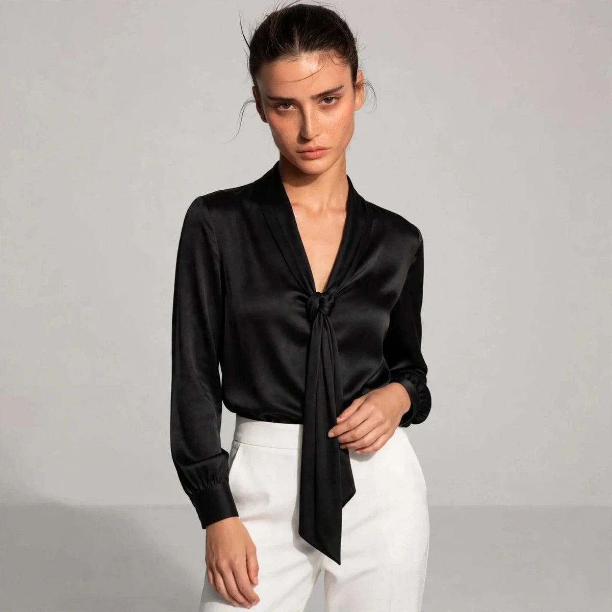 Woman wearing black satin tie-neck blouse with knotted front detail