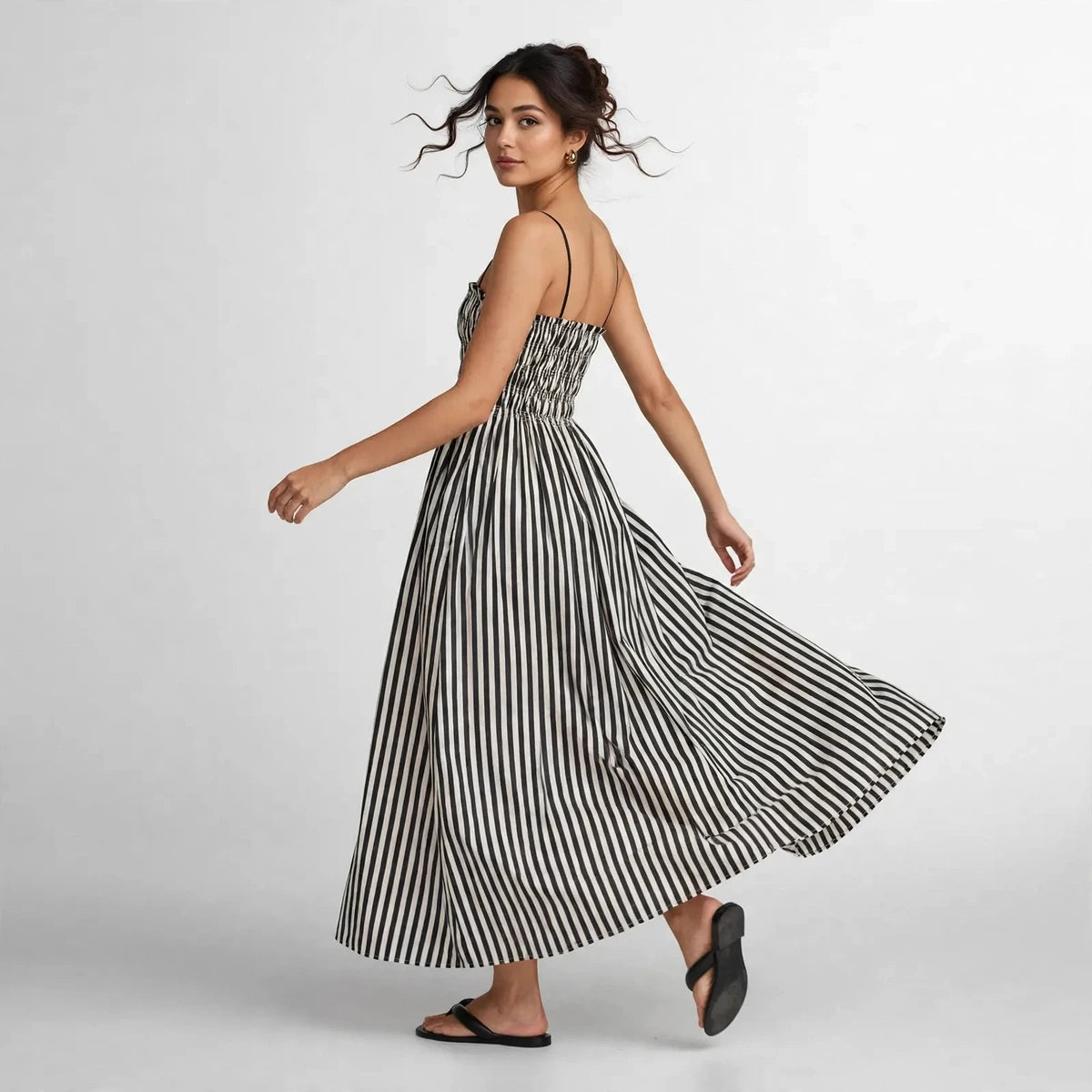 Model twirling in black and white striped smocked cami maxi dress with flowing skirt