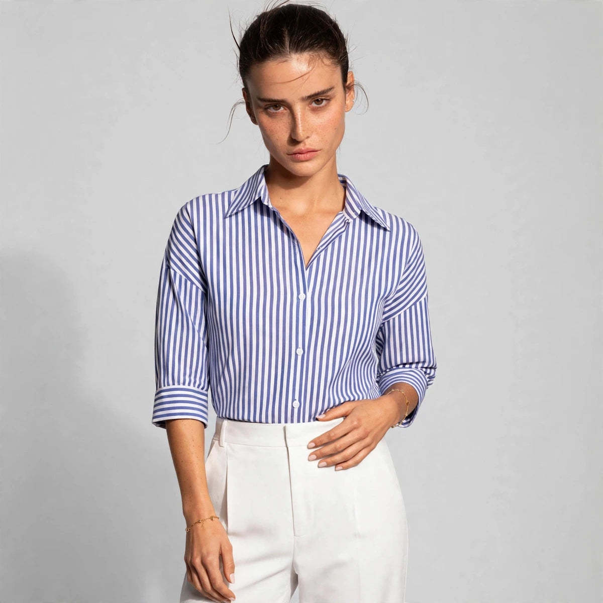 Woman wearing blue and white striped button-down shirt with white trousers, front view
