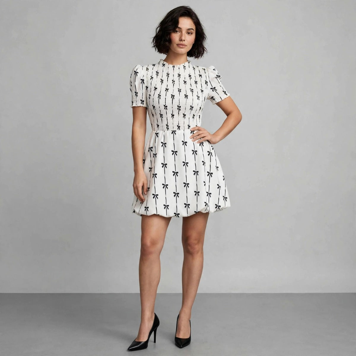 Front view of white mini dress with black bow print and smocked waist