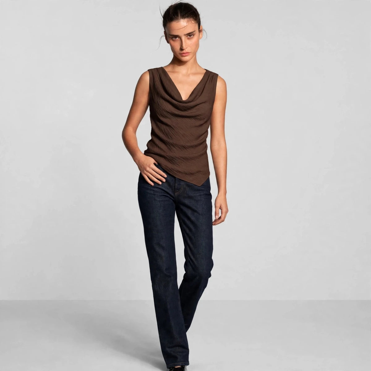 Model wearing a brown cowl neck tank top with dark jeans in a fashion editorial