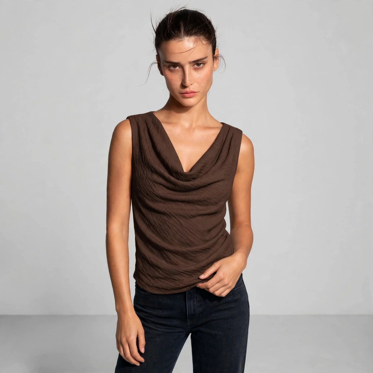 Woman wearing a brown sleeveless cowl neck tank top with draped fabric, front view