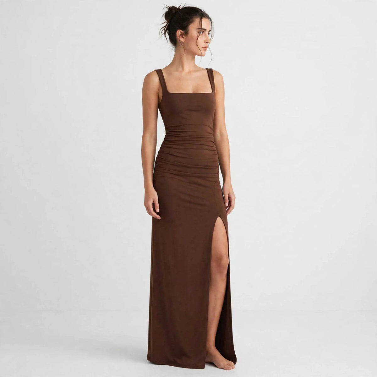 Woman wearing a brown ruched high-slit maxi dress, gazing to the side, front view