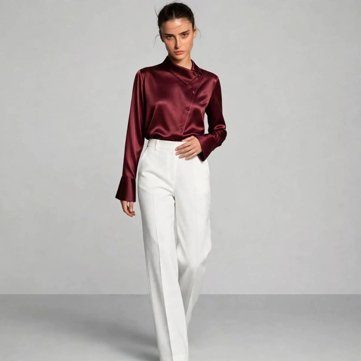 Model wearing burgundy satin collar blouse with white trousers in a fashion editorial