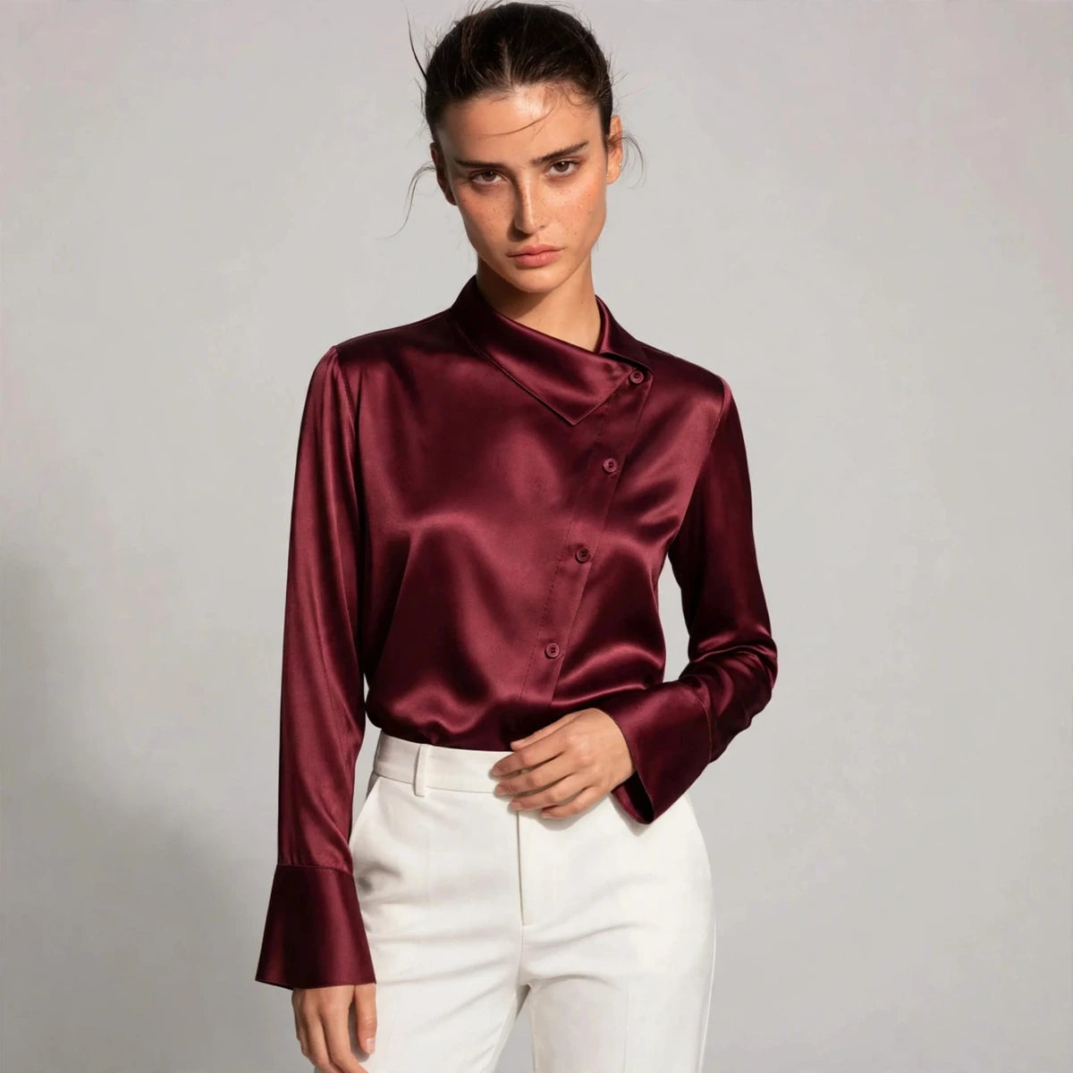 Woman wearing burgundy satin blouse with asymmetric collar and button front