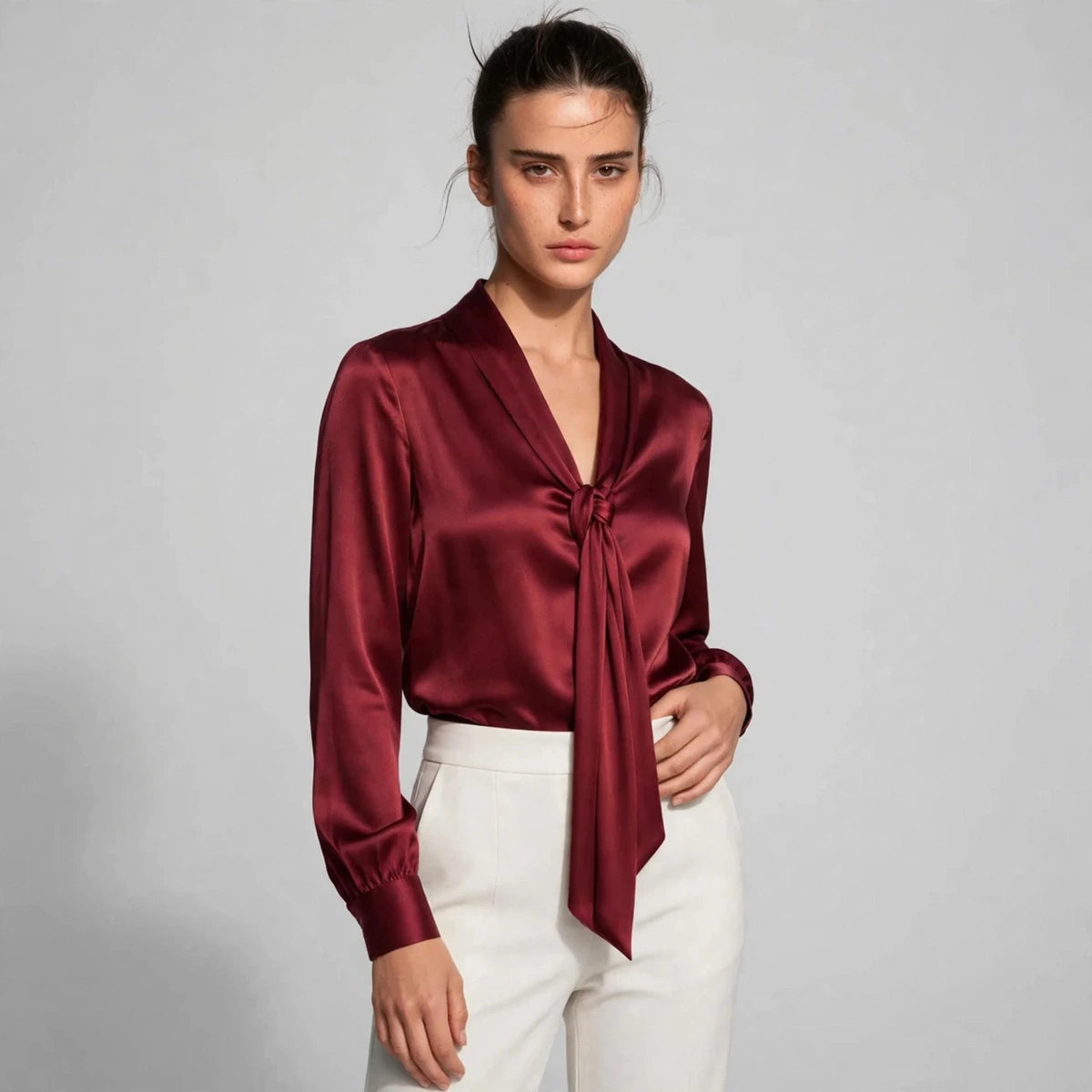 Woman wearing burgundy satin tie-neck blouse with knotted front detail