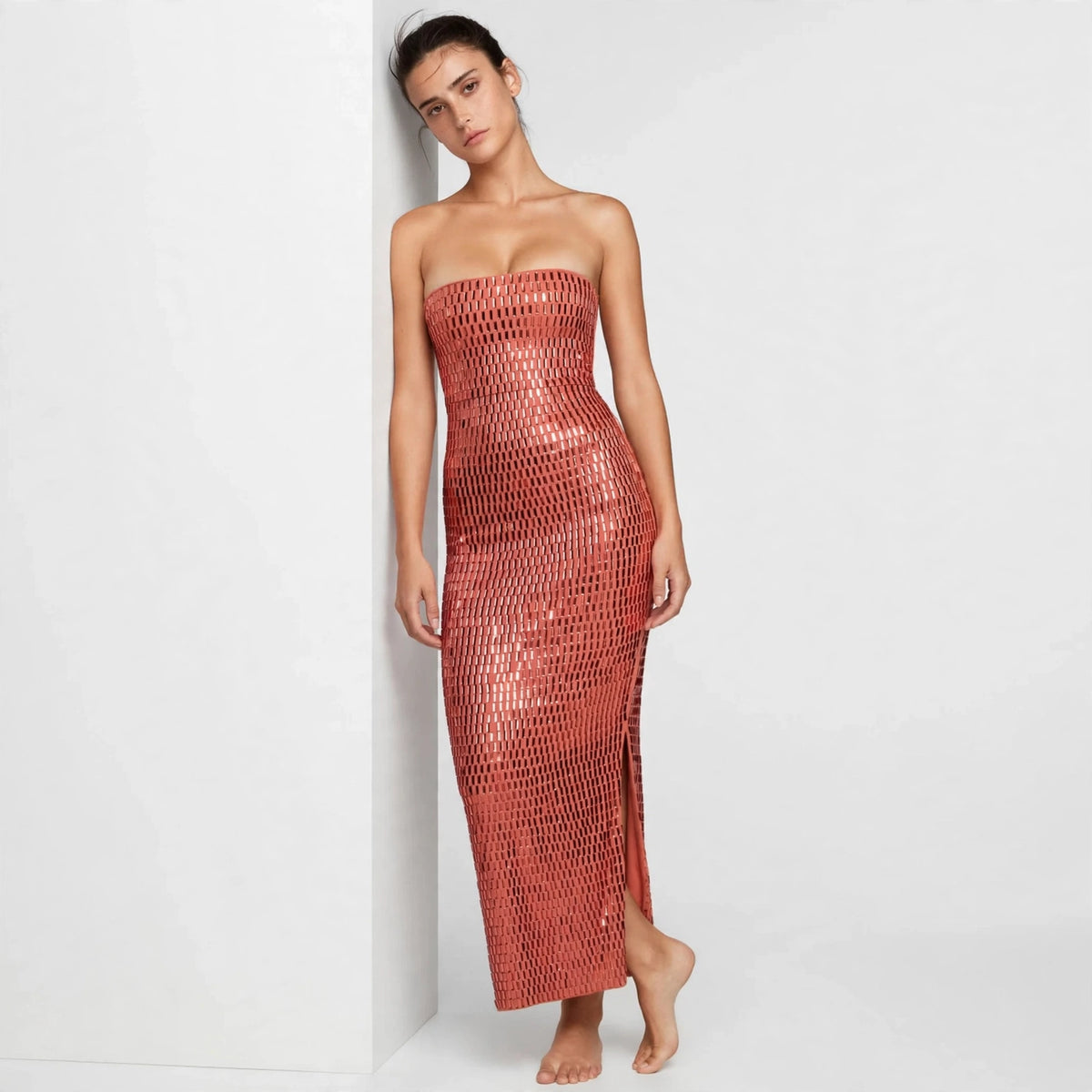 Model leaning against a wall in burnt coral sequin strapless tube maxi dress