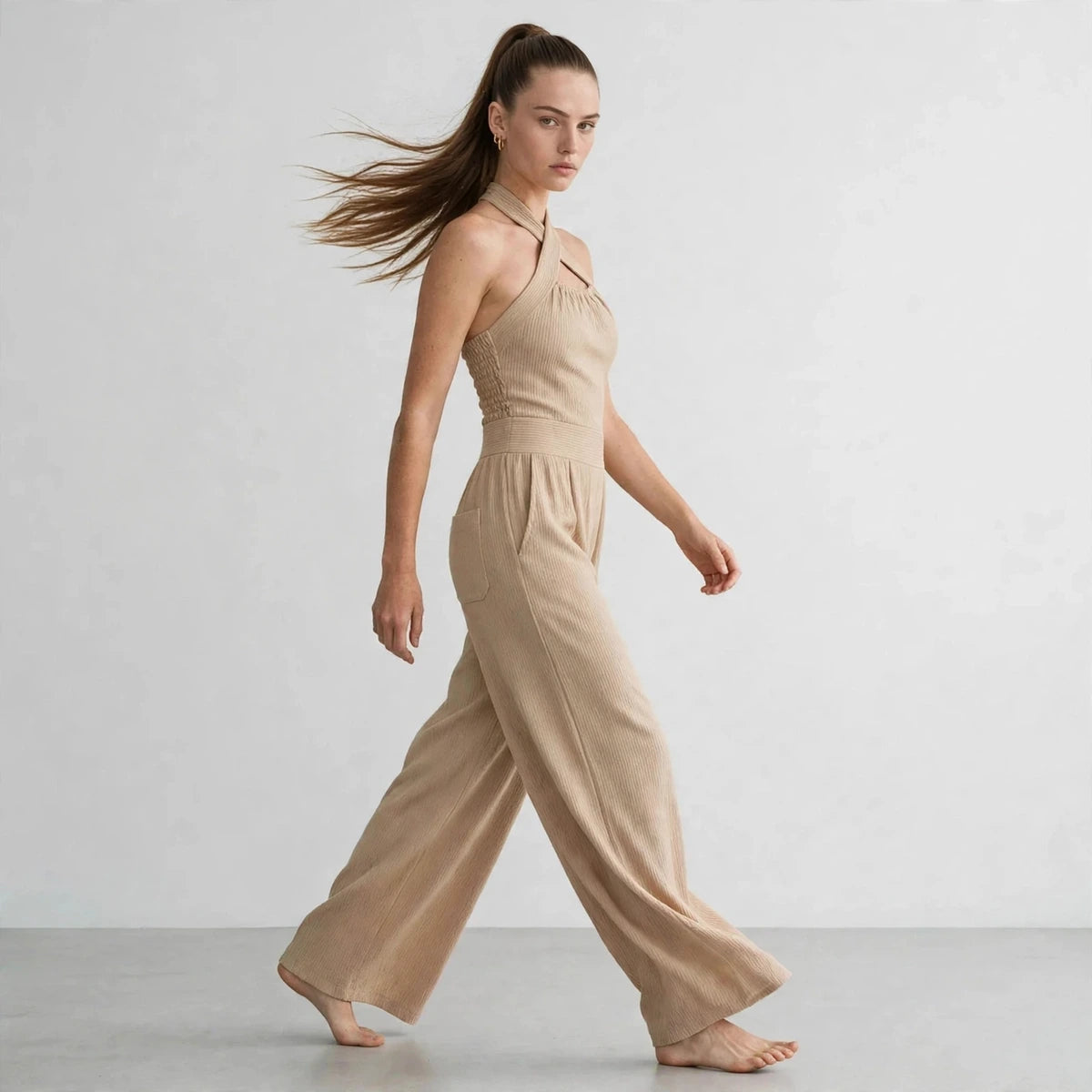 Side view of a beige crisscross halter jumpsuit with a flowing wide-leg fit