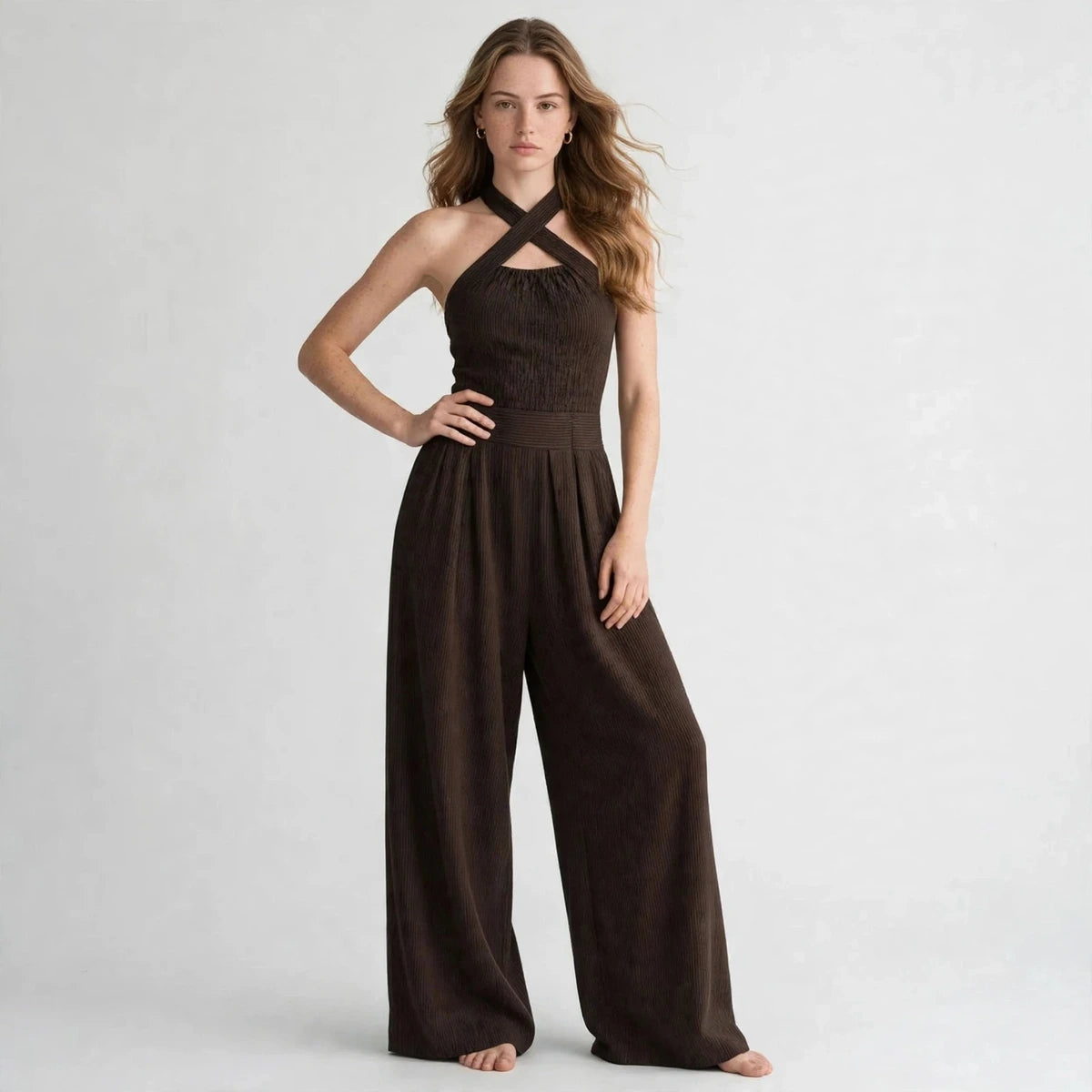 Woman wearing a dark brown crisscross halter jumpsuit with a ribbed waistband, front view