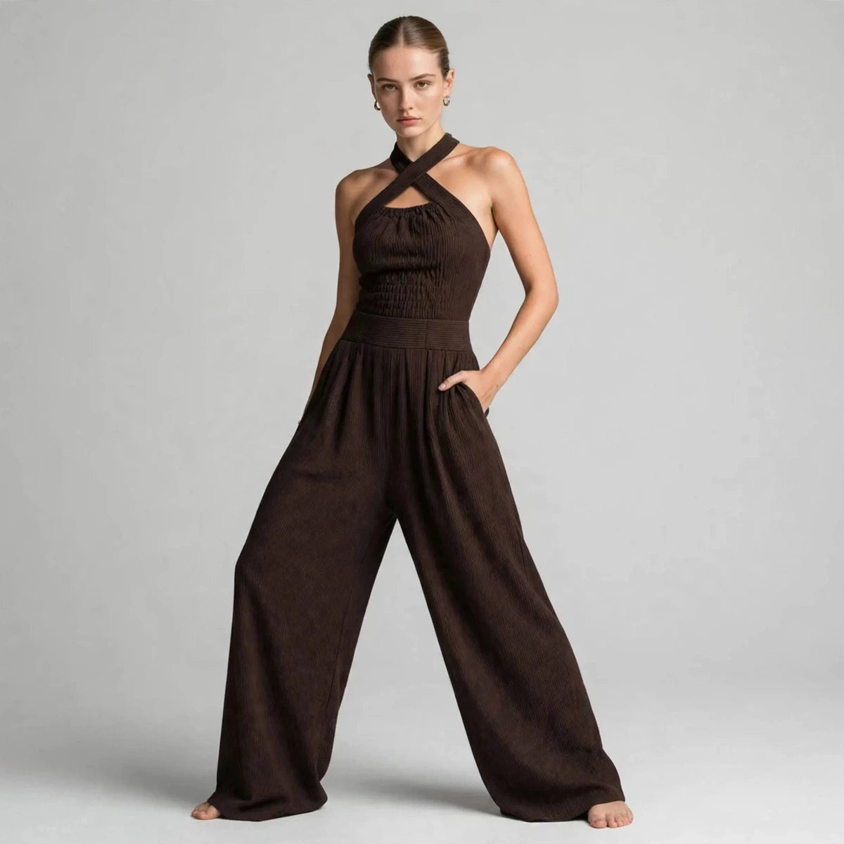 Woman in a dark brown crisscross halter jumpsuit in a wide stance, three-quarter view