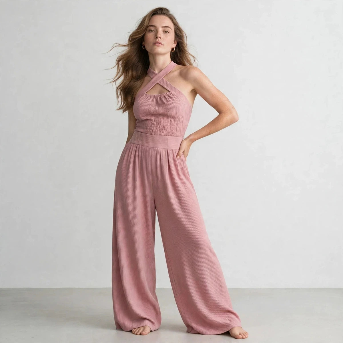 Woman wearing a dusty pink crisscross halter jumpsuit with a ribbed bodice, front view