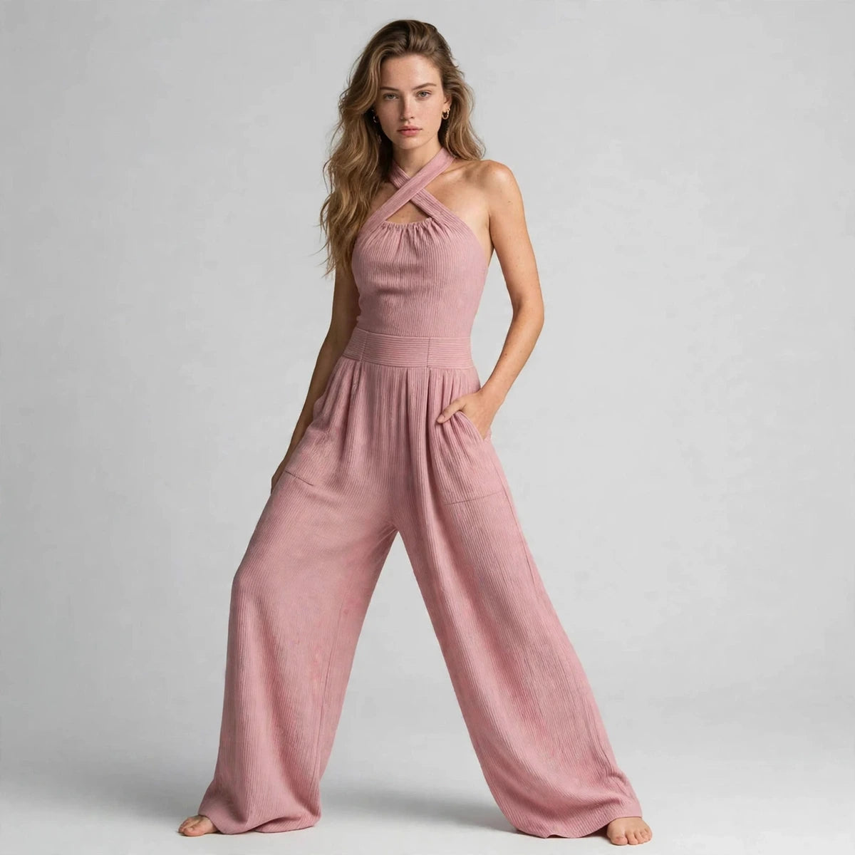 Woman in a dusty pink crisscross halter jumpsuit with hands in her pockets