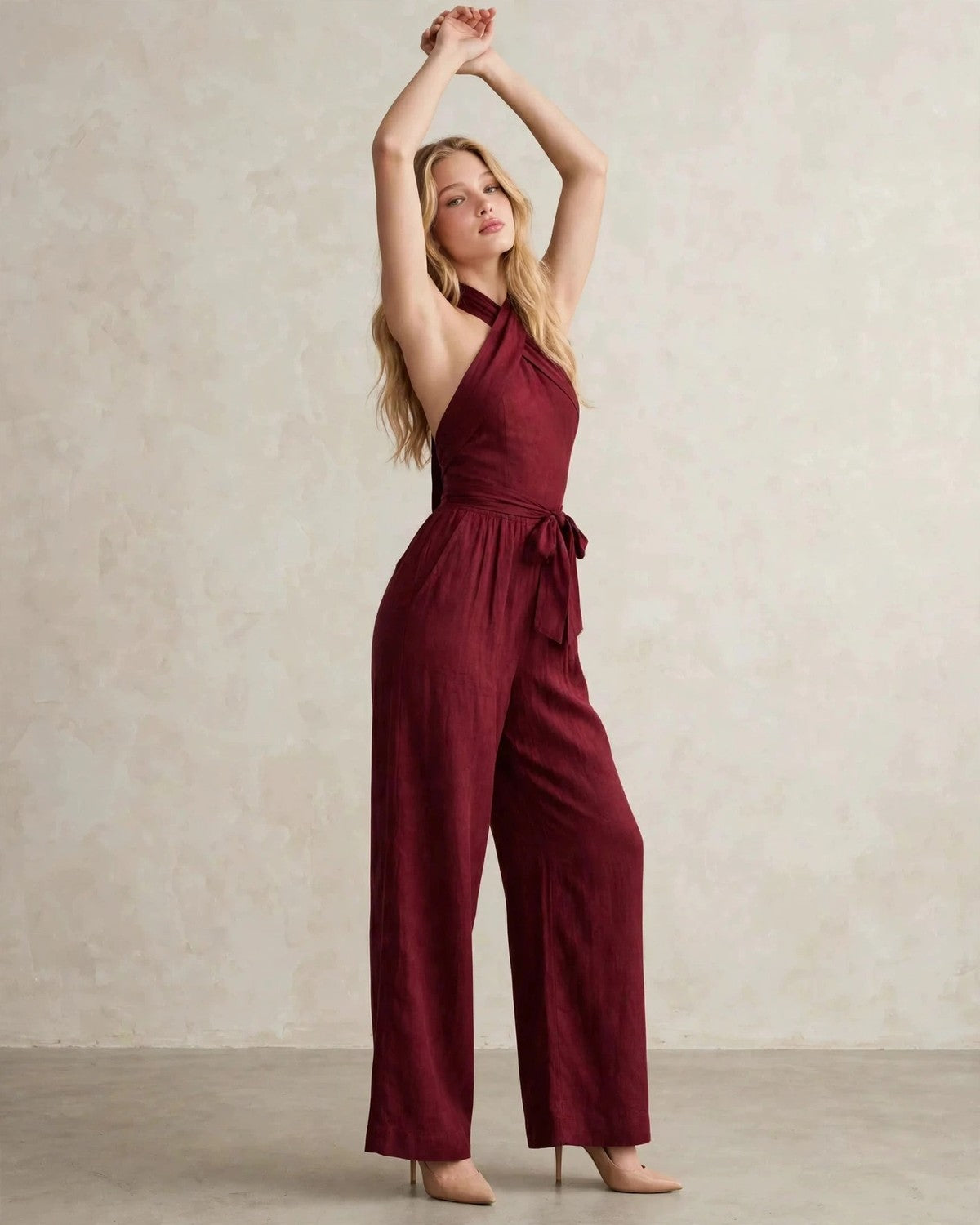 Women's halter neck wide-leg jumpsuit with waist tie in Wine Red, arms raised pose