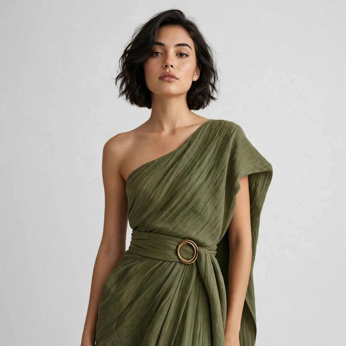 Close-up of a model in an army green draped one-shoulder dress with a wide belt and round ring buckle at the waist.