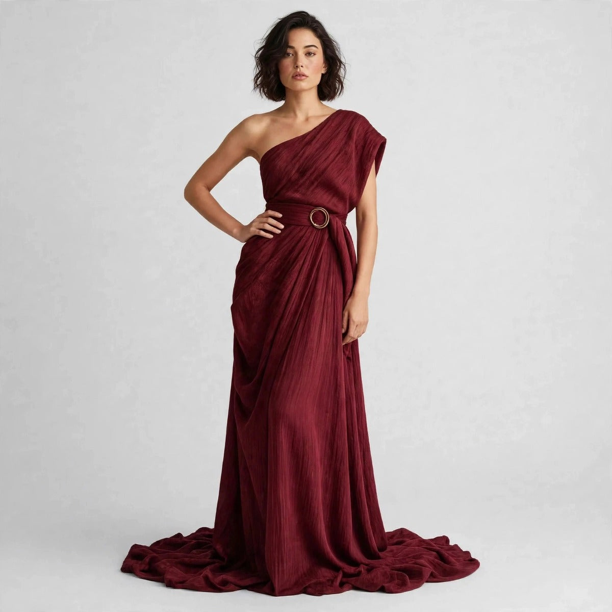 Model standing with hand on hip in a burgundy draped one-shoulder maxi dress with a belted ring buckle.