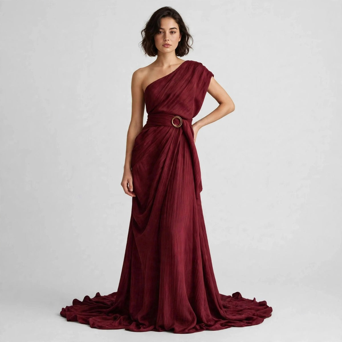 Full-length view of a model with hand on hip in a burgundy draped one-shoulder maxi dress with a belted ring buckle.