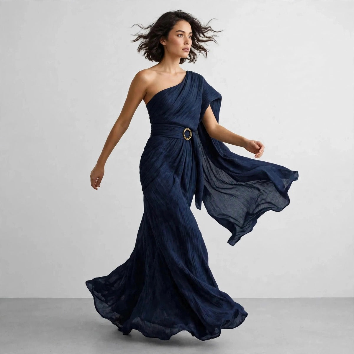 Model walking in navy blue draped one-shoulder maxi dress with flowing skirt