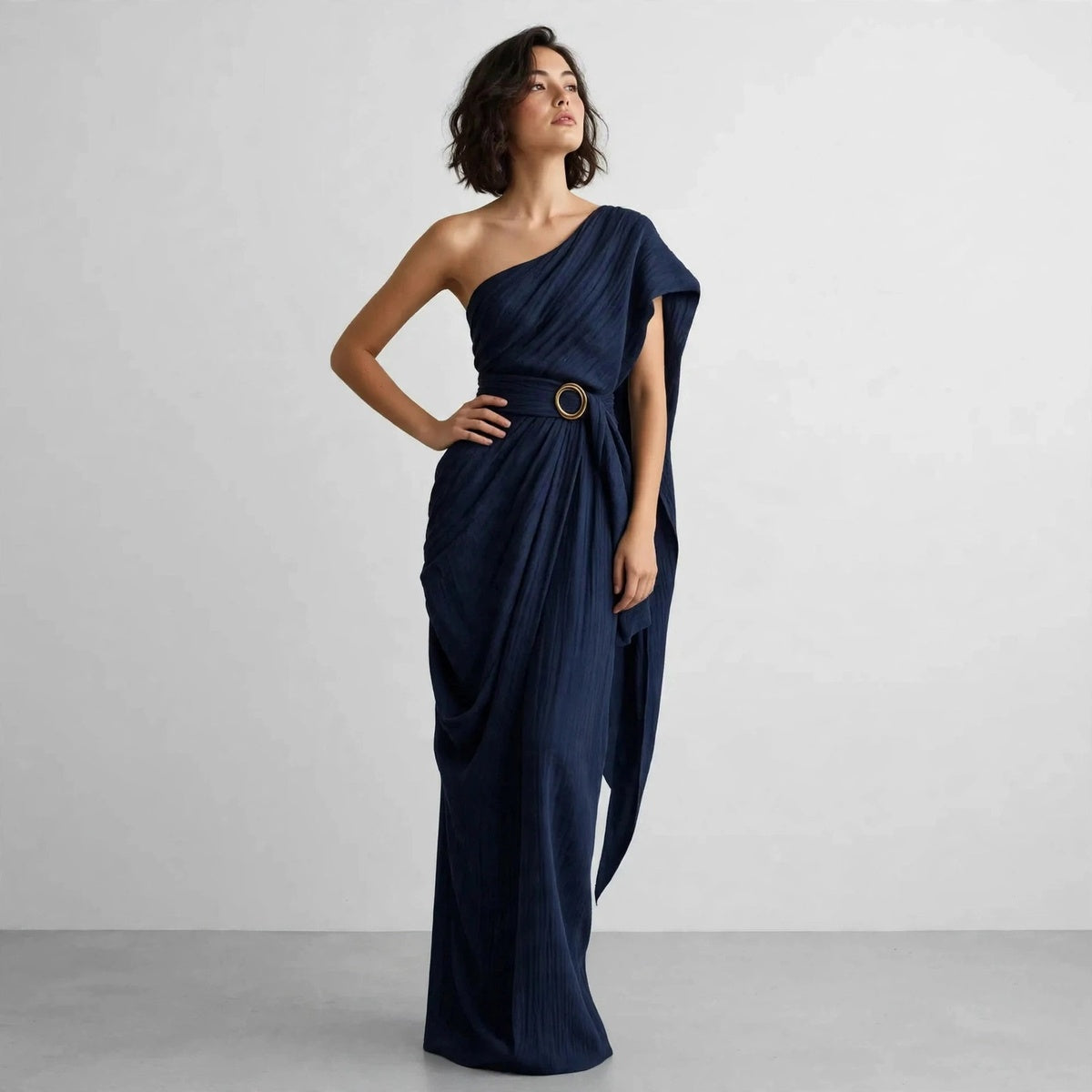 Model wearing navy blue draped one-shoulder maxi dress in a studio editorial