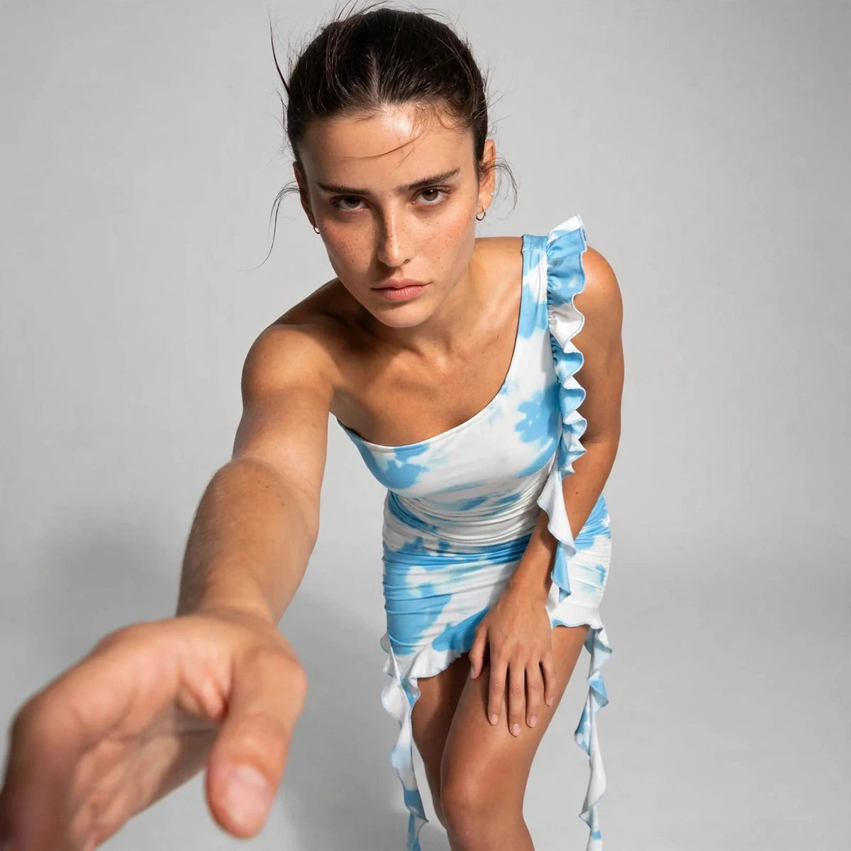 Model wearing blue tie-dye ruffled one-shoulder mini dress in a fashion editorial