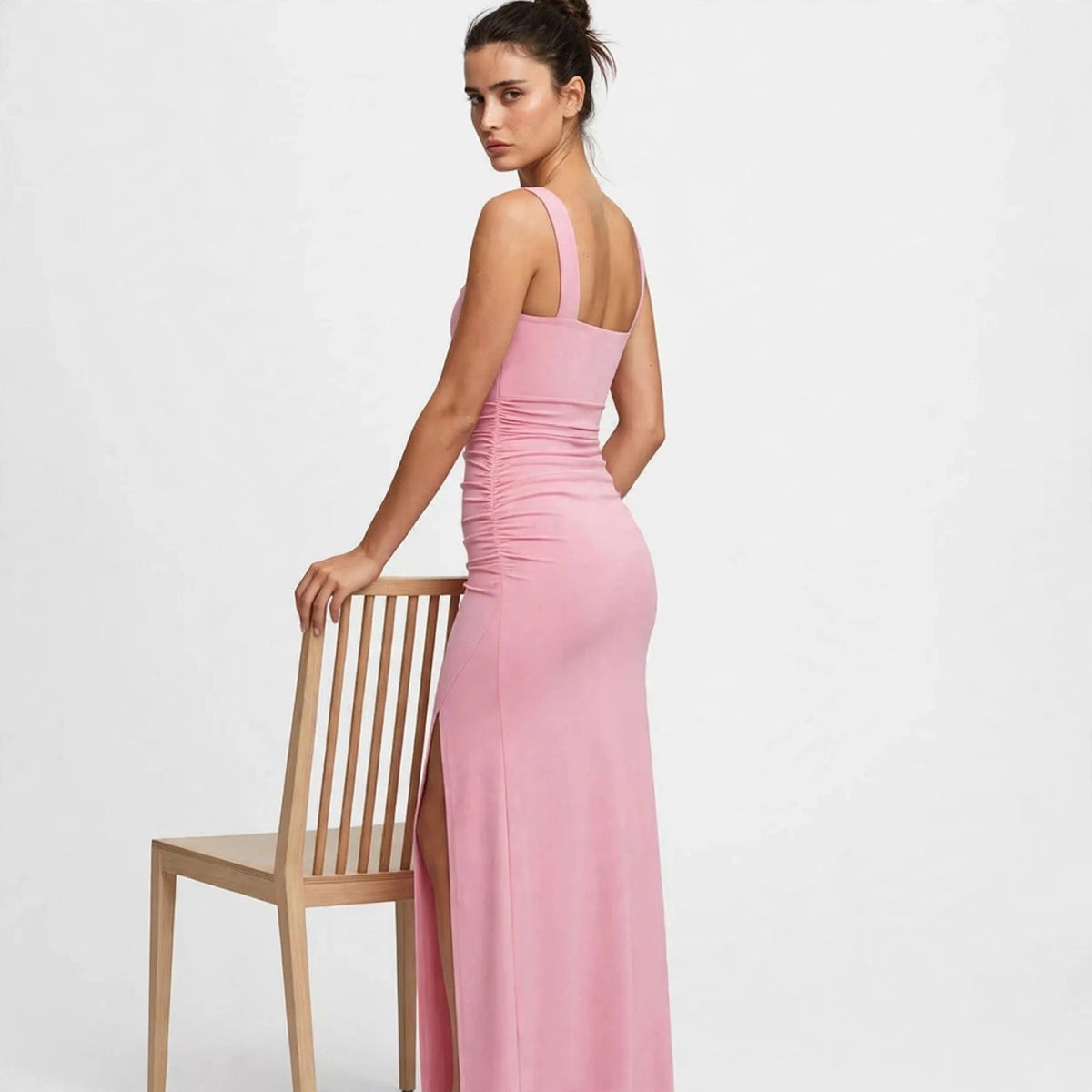 Back view of a pink ruched high-slit maxi dress, model leaning on a chair