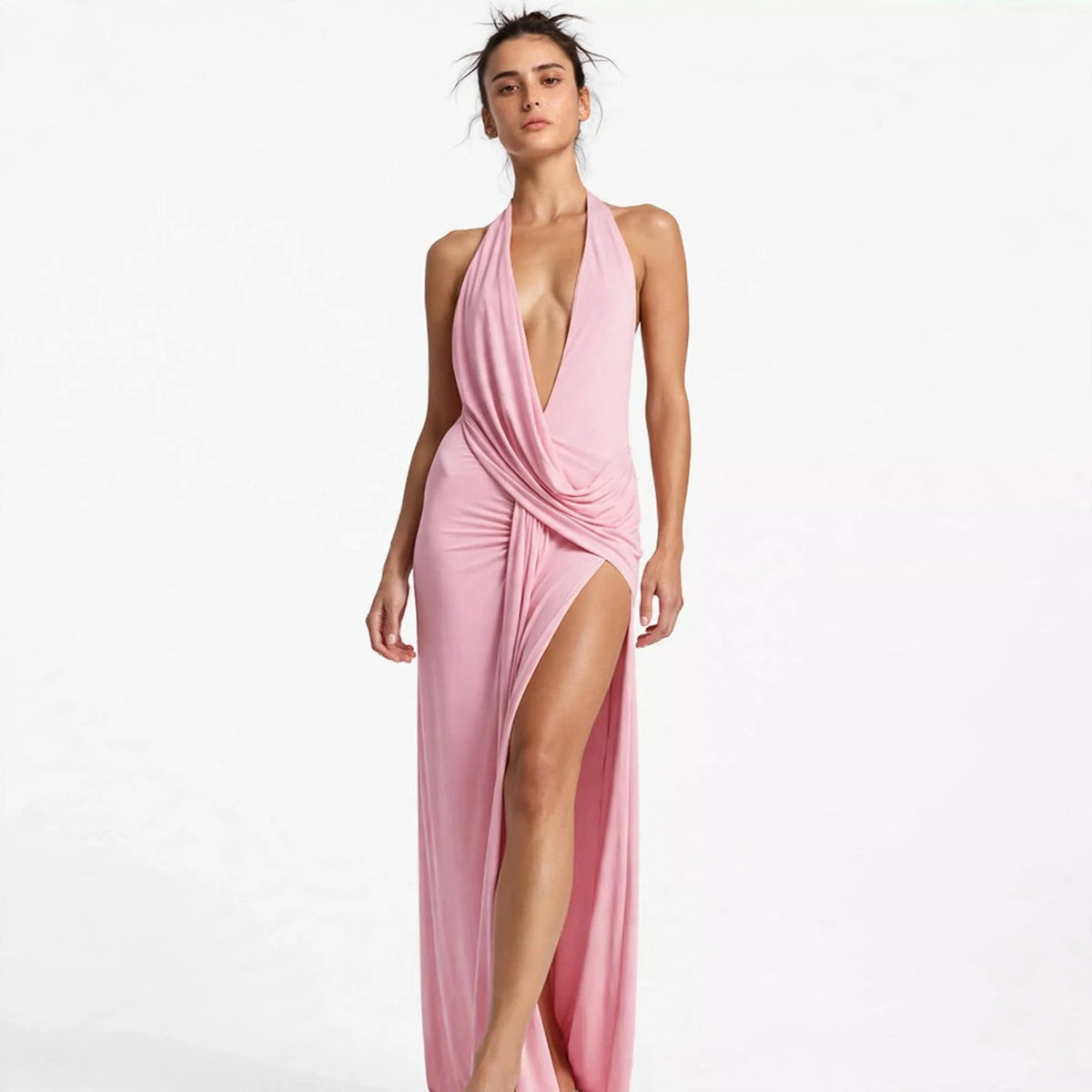 Woman wearing pink backless halter maxi dress with thigh-high slit, front view