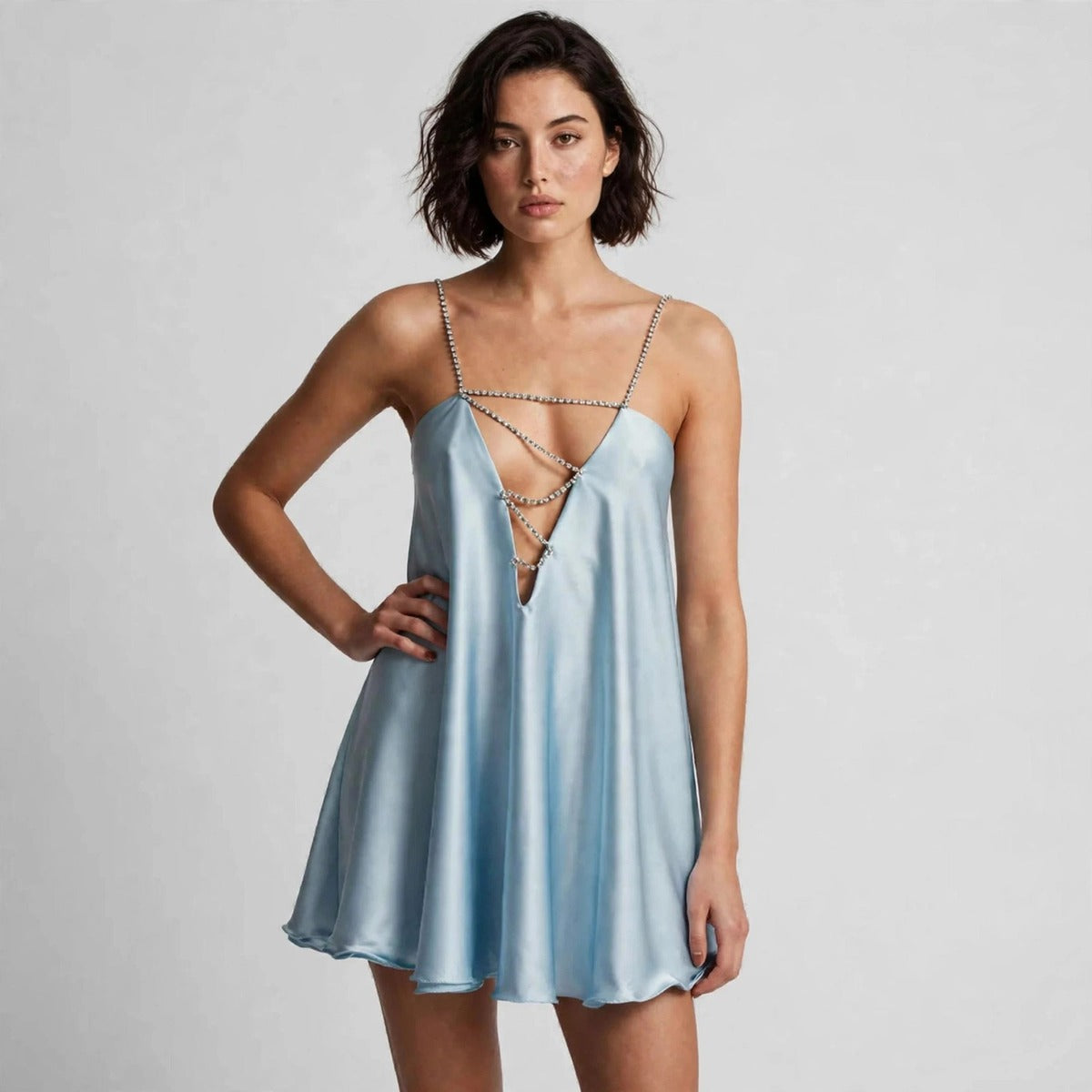Woman standing with hand on hip in a light blue satin slip mini dress with silver chain details at the neckline.