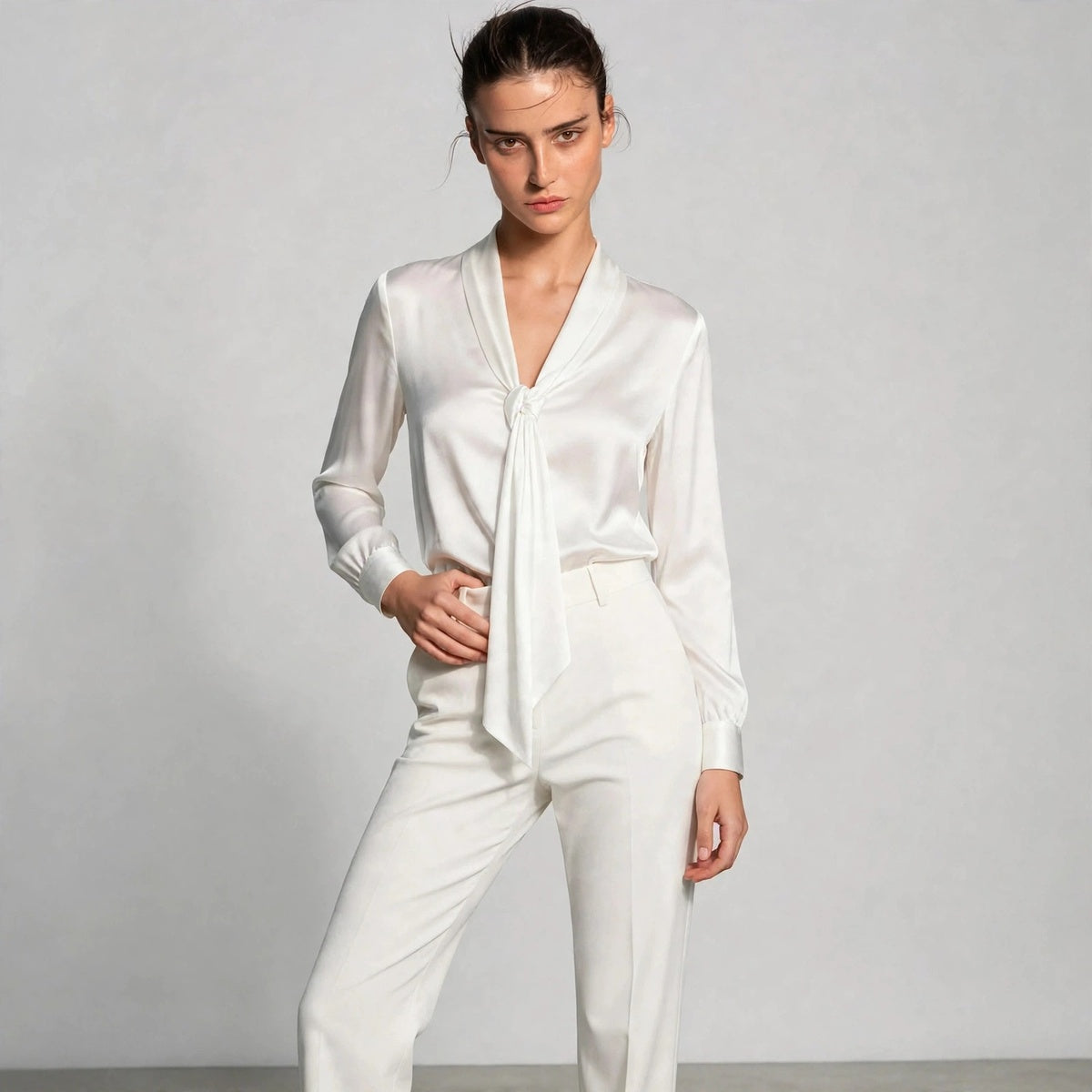 Model wearing white satin tie-neck blouse with white trousers in a fashion editorial