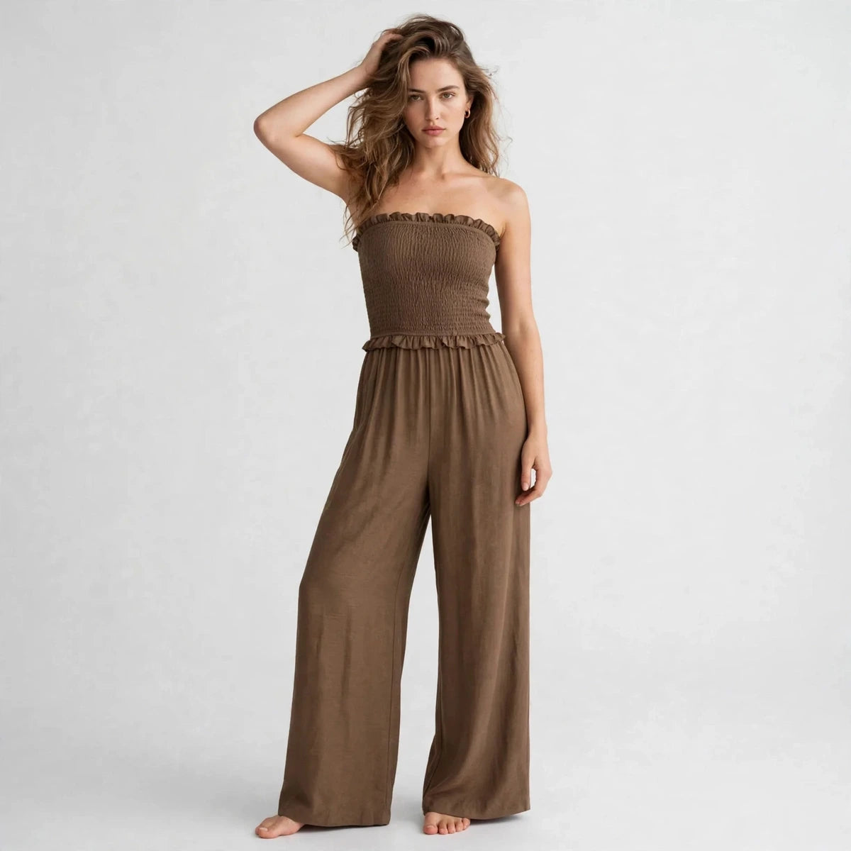 Model posing in brown smocked strapless jumpsuit with ruffle trim, editorial front view