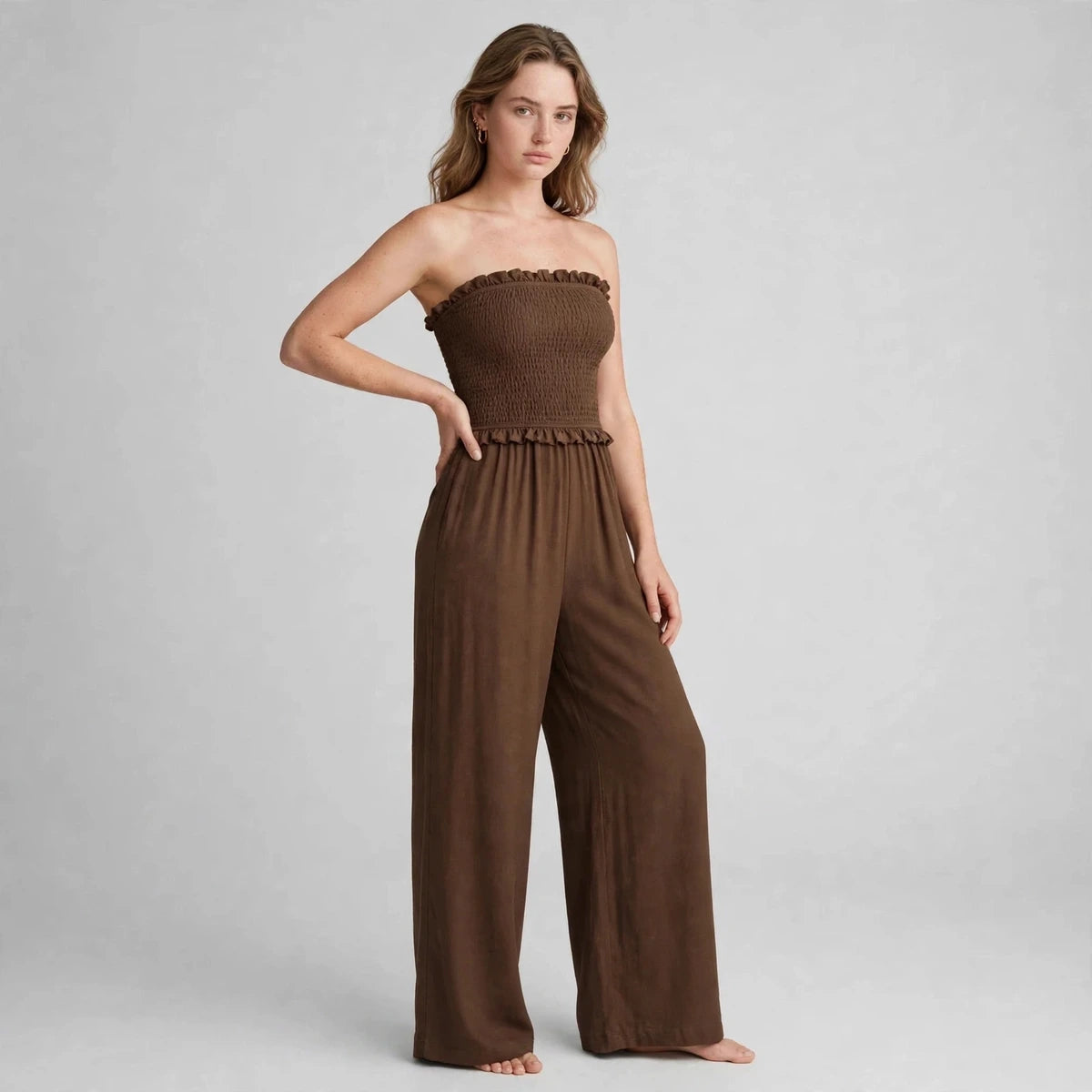 Woman wearing brown smocked strapless jumpsuit with wide-leg pants, three-quarter view