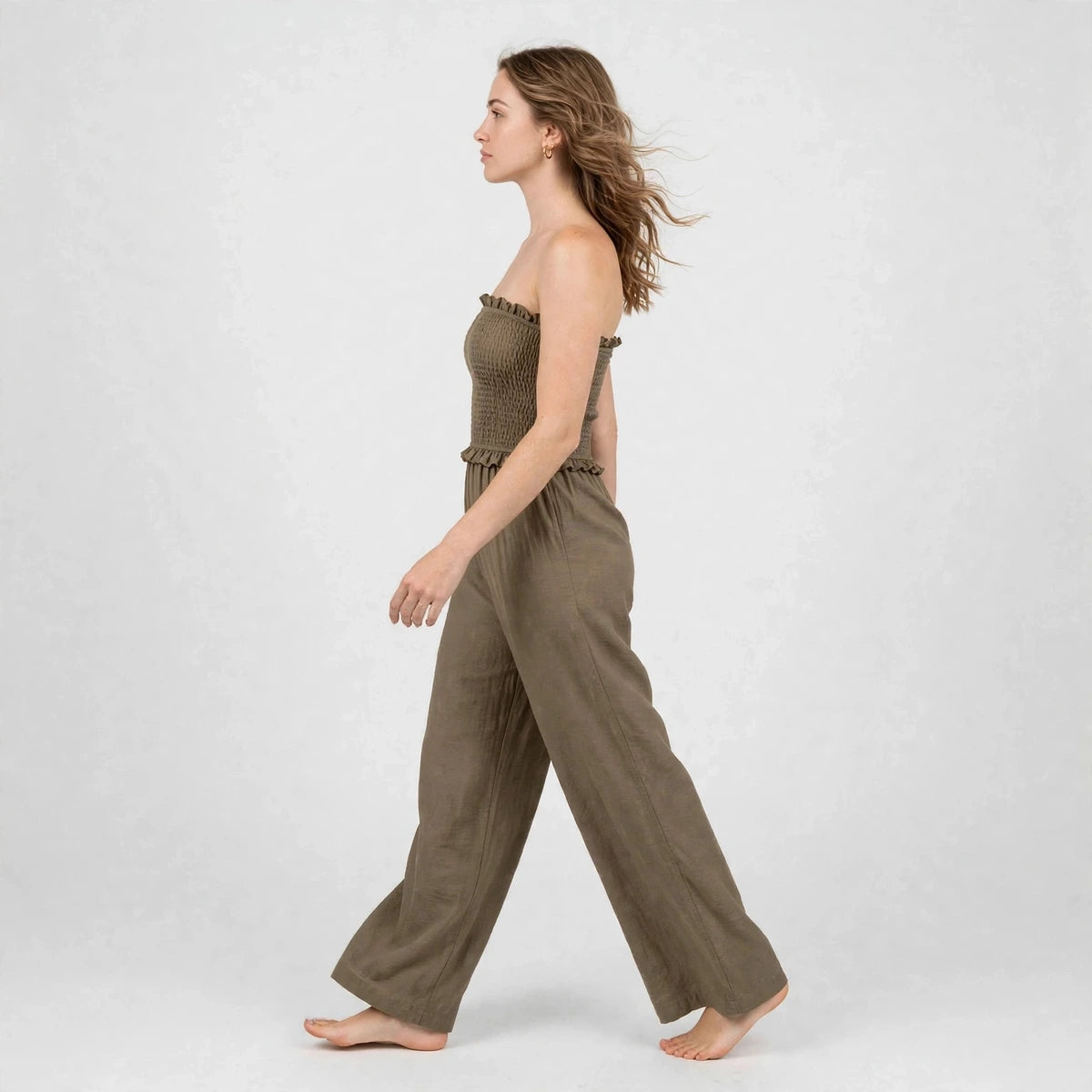 Model walking in brown smocked strapless jumpsuit with wide-leg pants, side view
