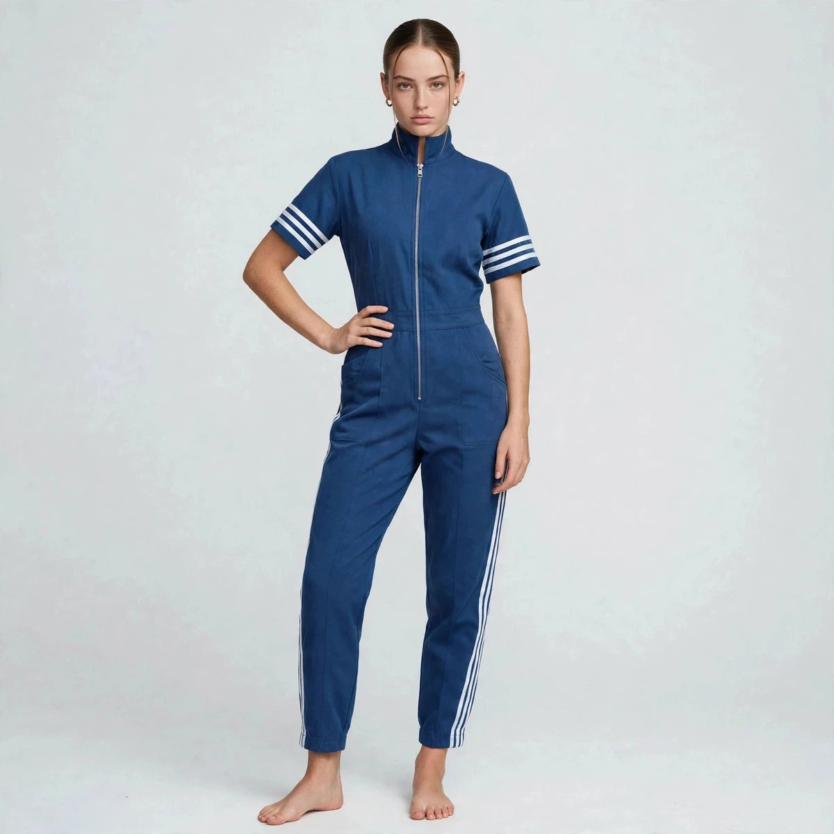 Model in blue sporty stripe zip-front jumpsuit with hand on hip, front view