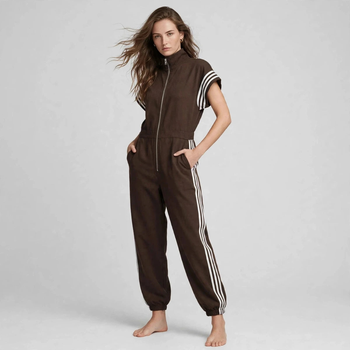 Model in brown sporty stripe zip-front jumpsuit with hands in pockets, front view