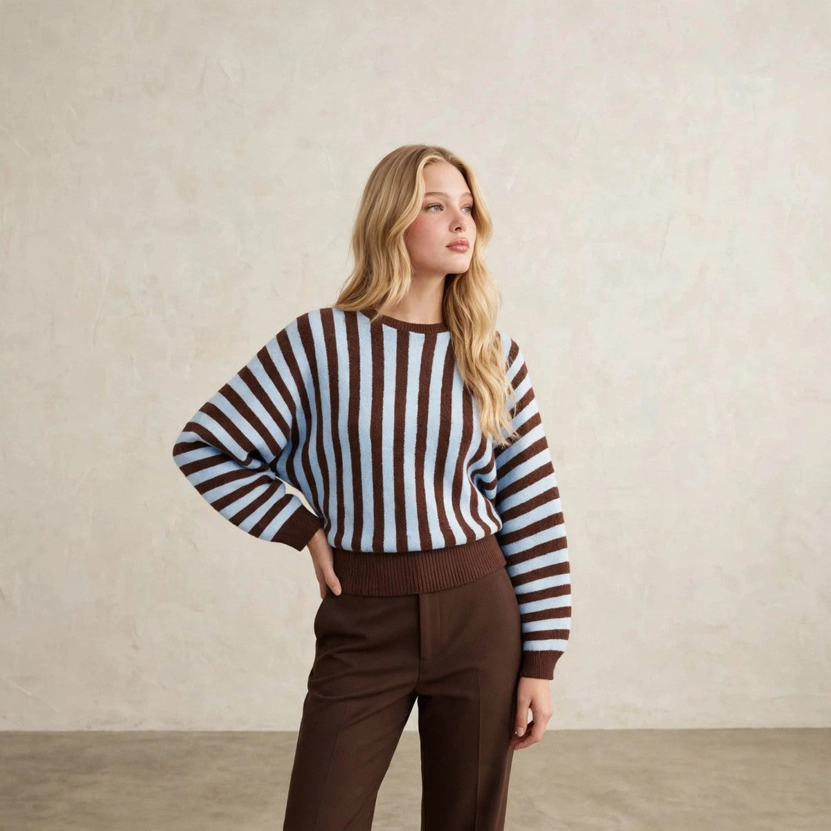 Women's light blue and brown vertical striped crew neck sweater, hand on hip pose