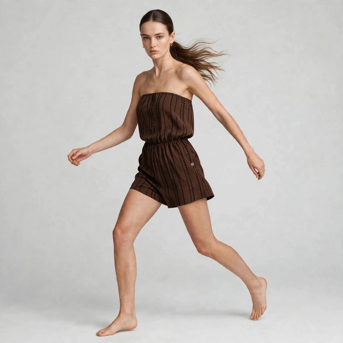 Model mid-stride in brown striped strapless tube romper, editorial fashion shot