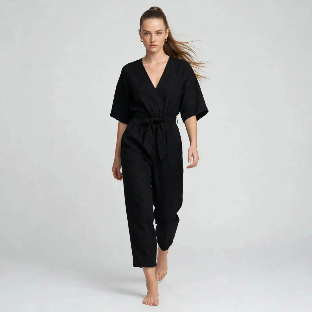 Model walking in black V-neck tie waist jumpsuit, editorial fashion shot