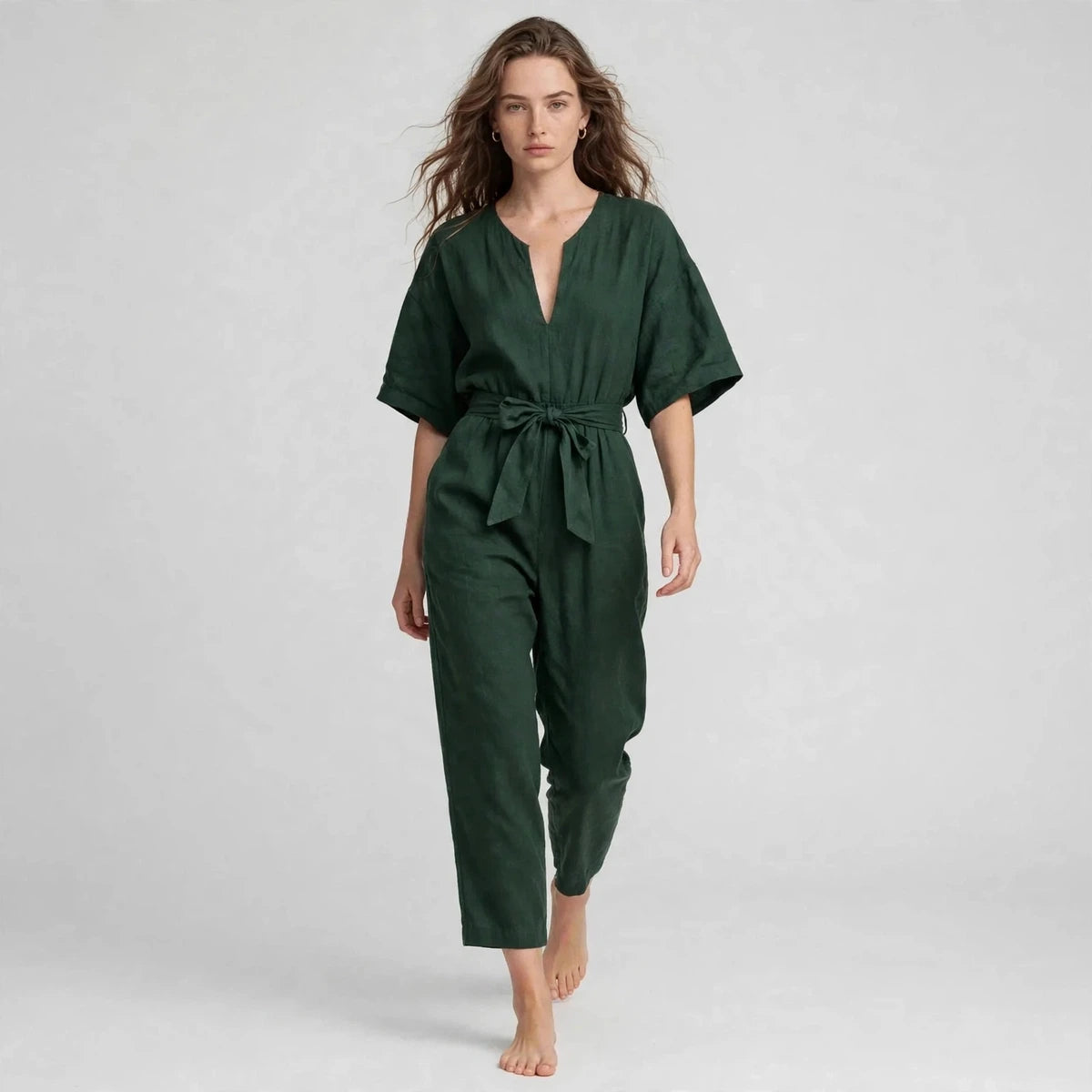 Model walking in dark green V-neck tie waist jumpsuit, editorial fashion shot