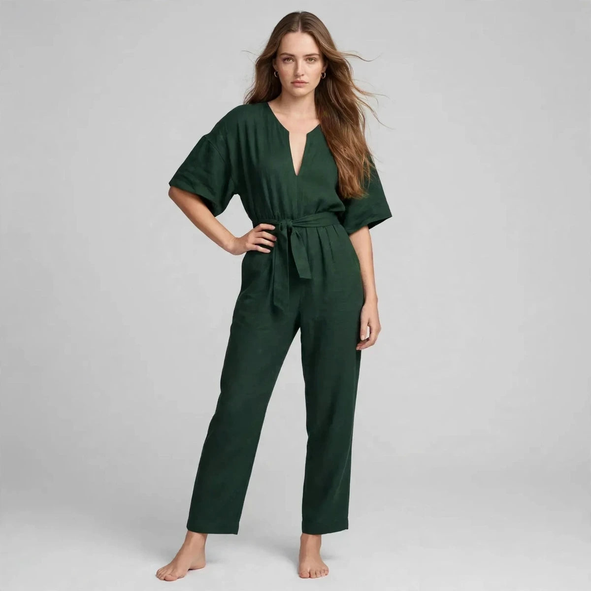 Woman wearing dark green V-neck tie waist jumpsuit with short sleeves, front view
