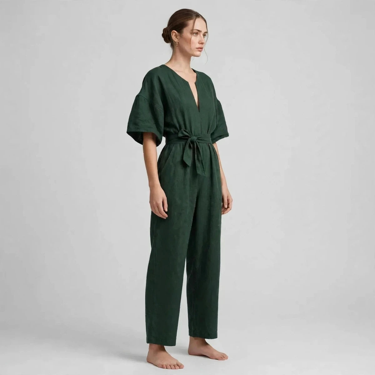 Side view of dark green V-neck tie waist jumpsuit with tied belt