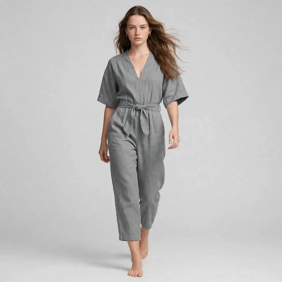 Model walking in gray V-neck tie waist jumpsuit, editorial fashion shot