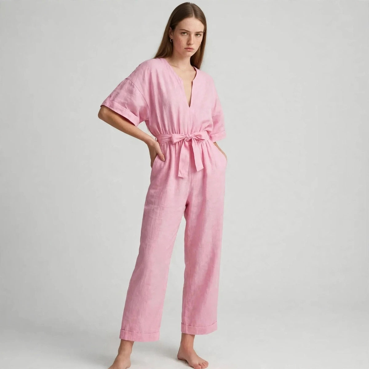 Model wearing pink V-neck tie waist jumpsuit with hands in pockets, front view