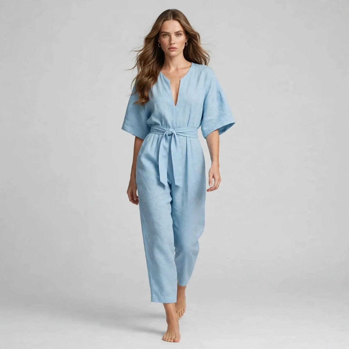 Model walking in sky blue V-neck tie waist jumpsuit, editorial fashion shot