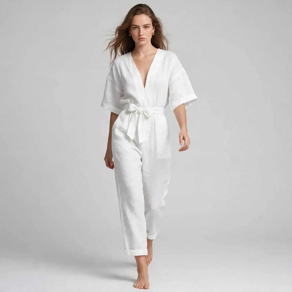Model walking in white V-neck tie waist jumpsuit, editorial fashion shot