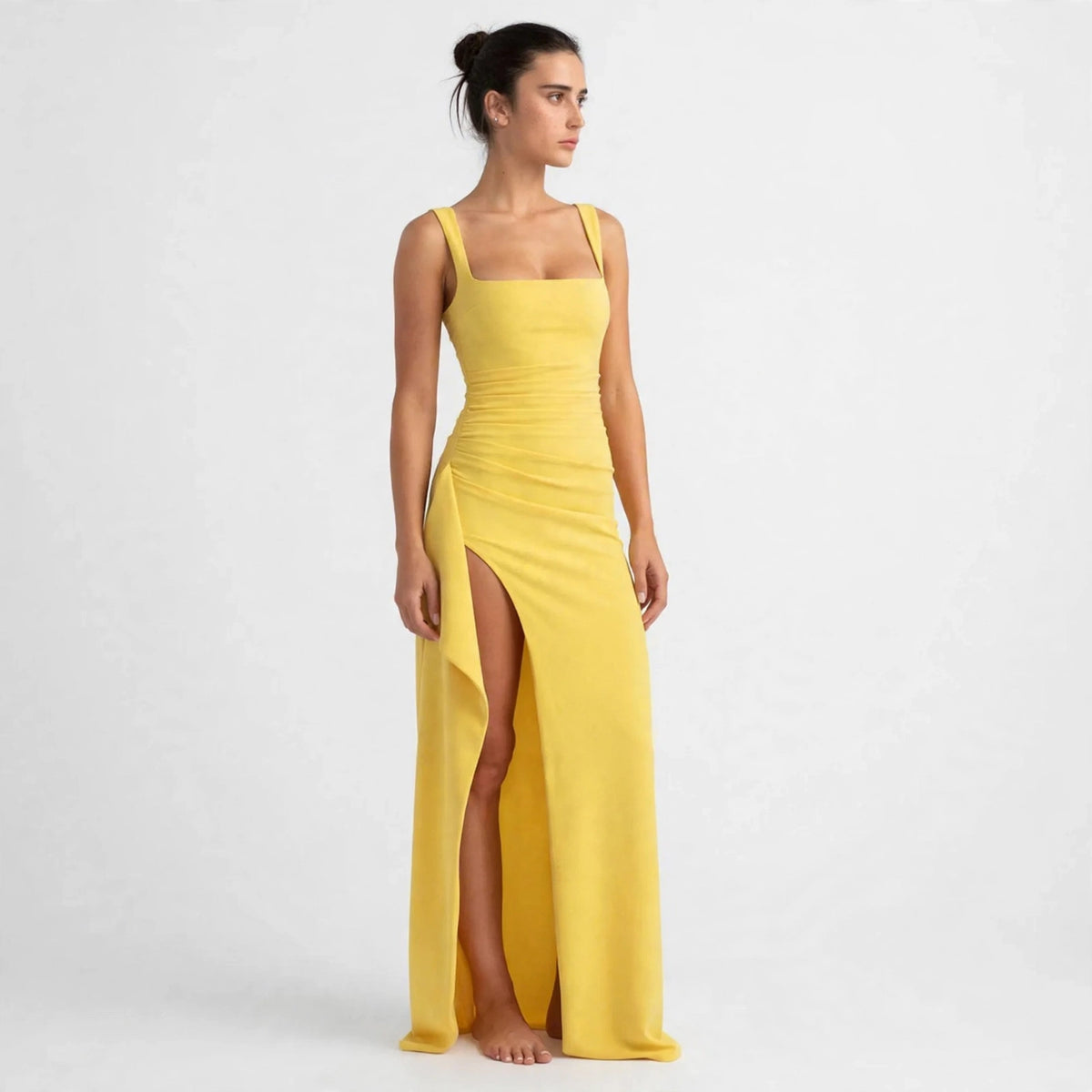 Woman wearing a yellow ruched high-slit maxi dress with square neckline, front view